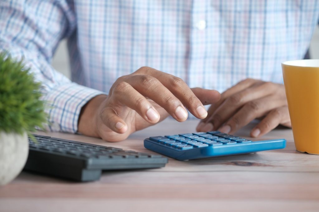 Persona realizando cálculos con una calculadora junto a una computadora